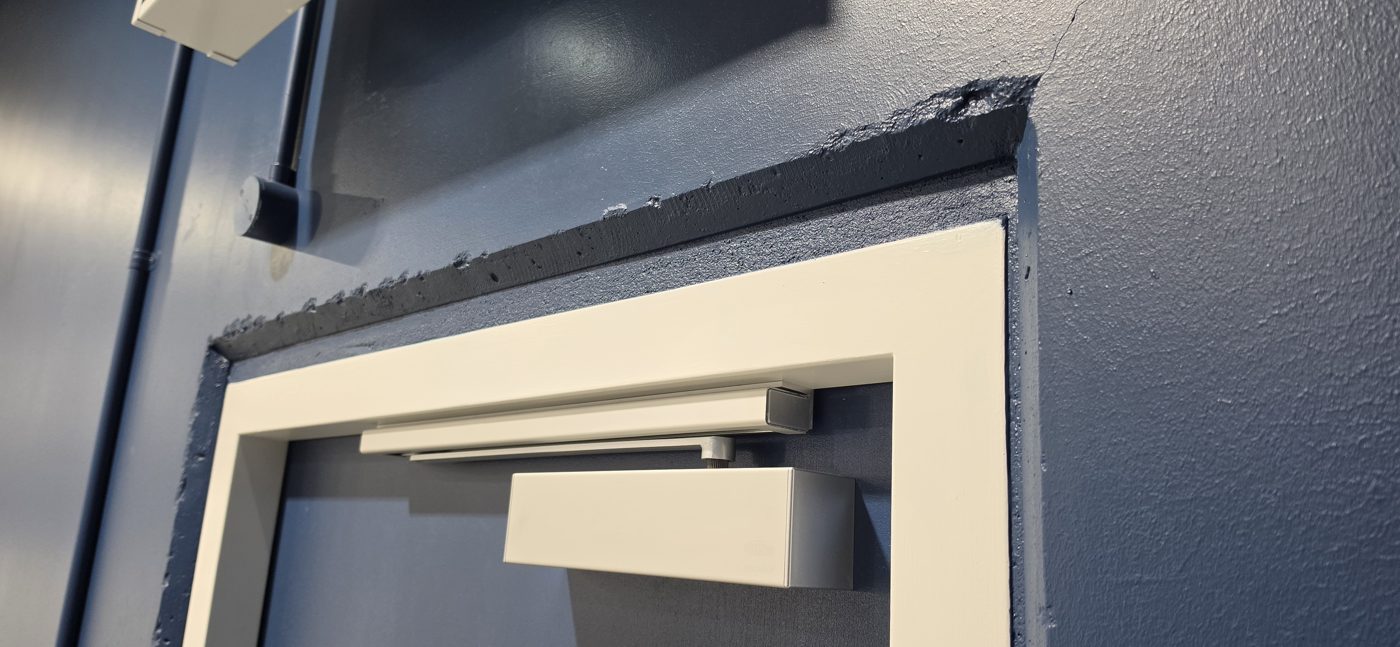 Finished frame head detail — door closers fitted, clean lines into the existing wall